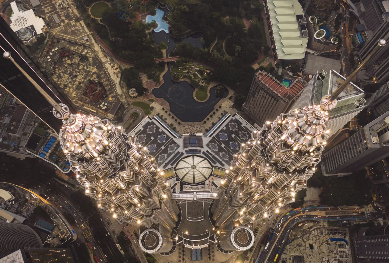 Aerial view down the illuminated Petronas Twin Towers toward KLCC Park.